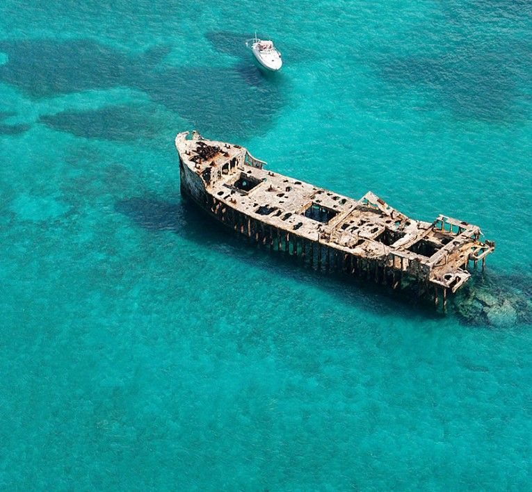 A rusted shipwreck floating in bright turquoise water, with a small boat nearby.