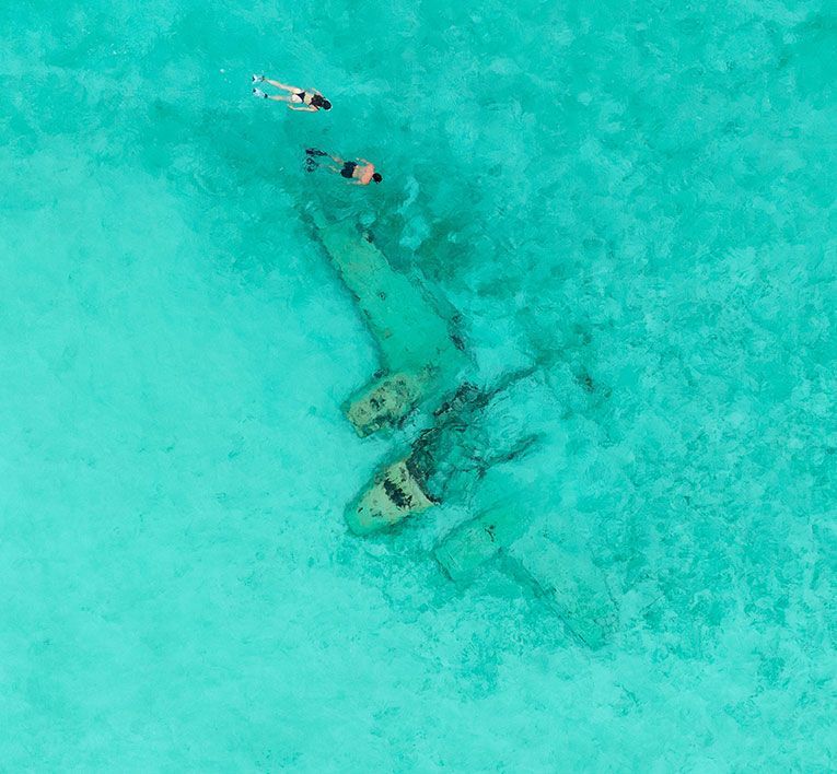 Two people kayaking over a turquoise ocean above a sunken shipwreck