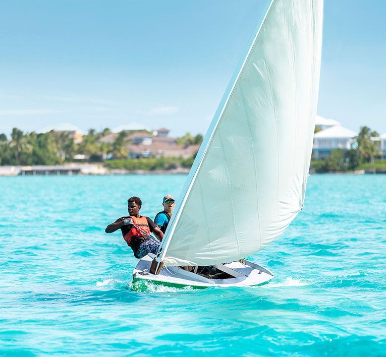 Two sailors on a small sailboat racing across bright turquoise water near shore