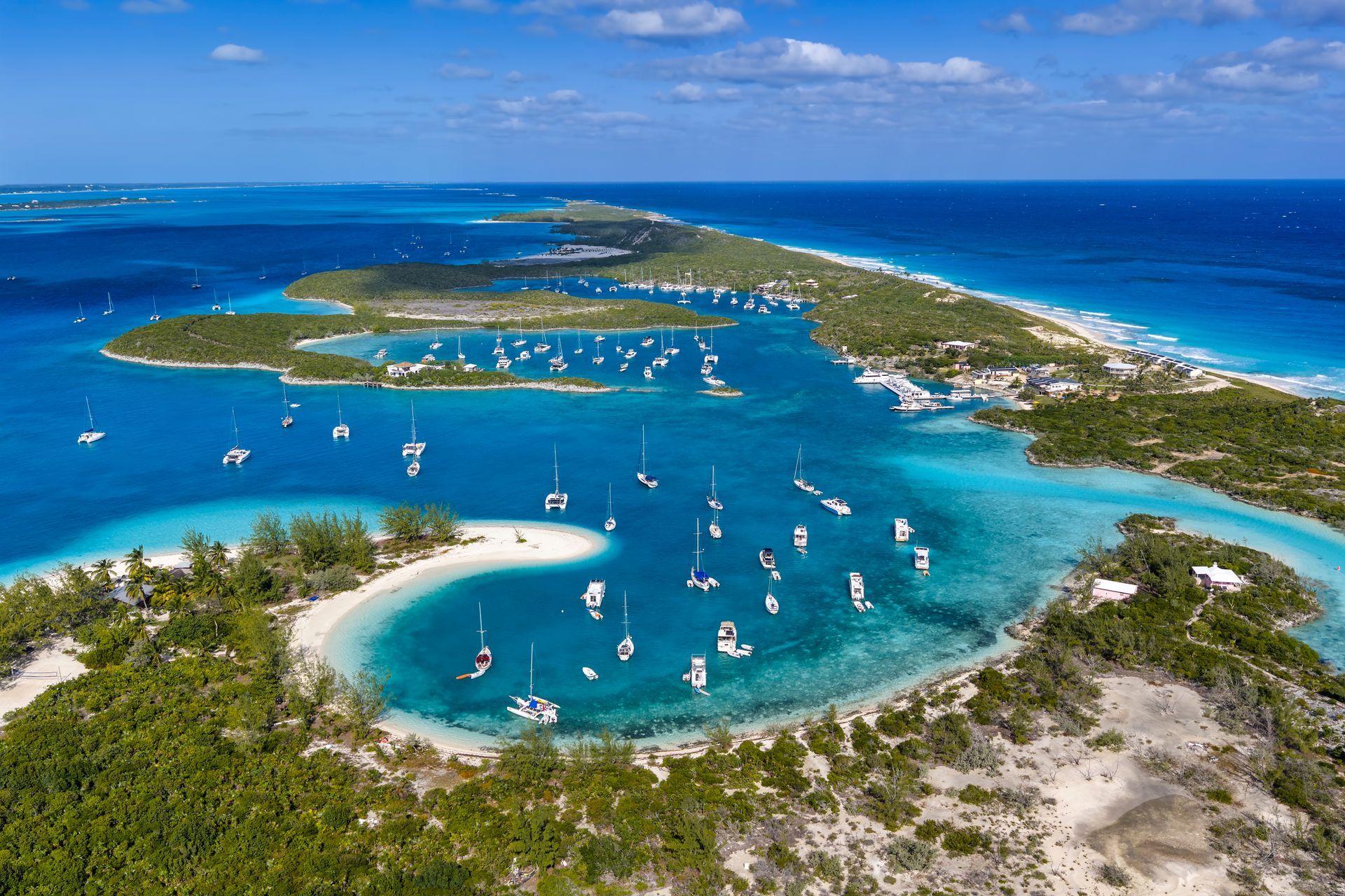 Aerial view of turquoise lagoon with sailboats, white sandbars, and a small island under a blue sky