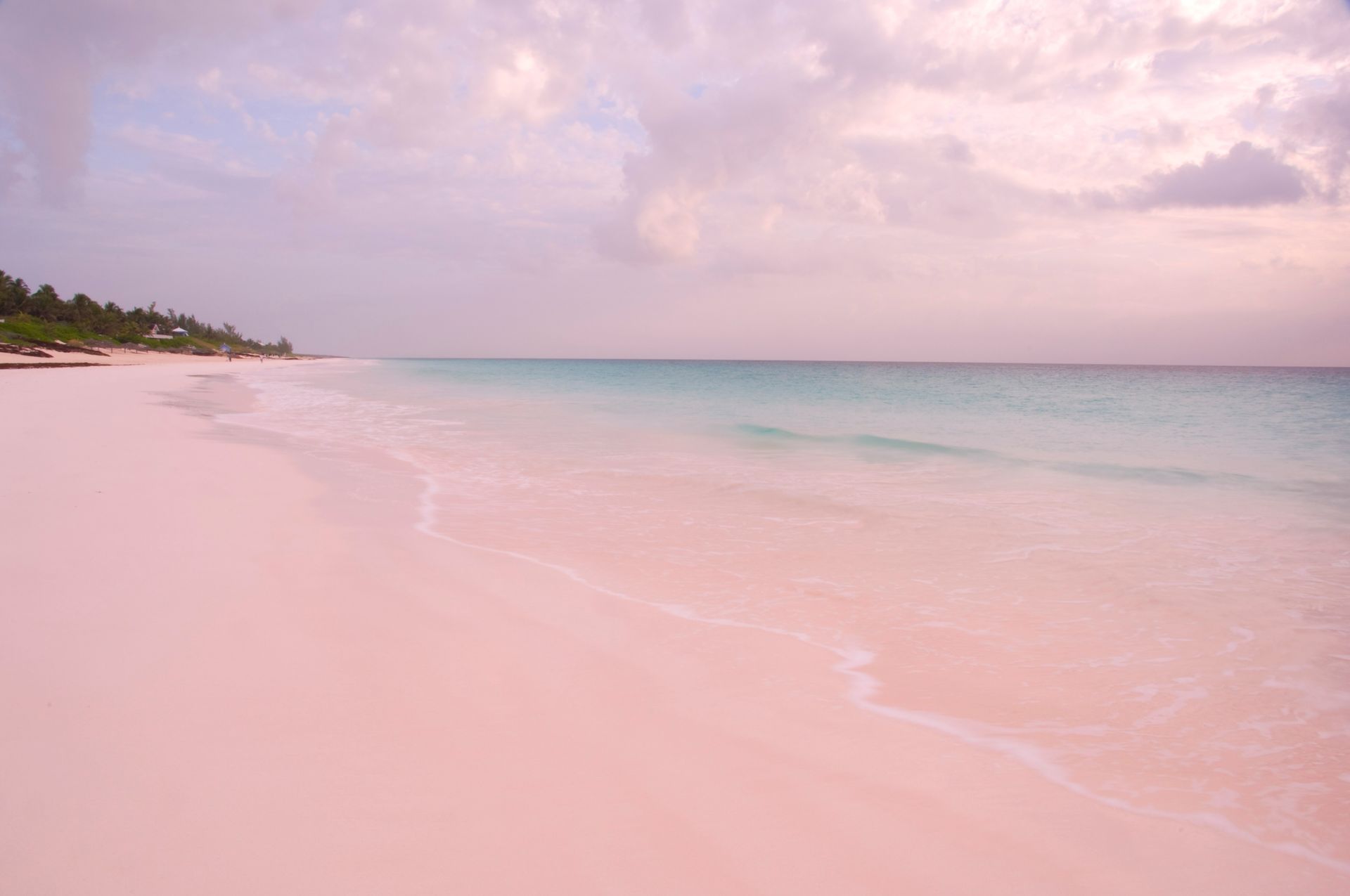 Pink sandy beach with calm turquoise water and a pastel cloudy sky