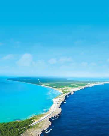 Aerial view of a narrow tropical island with turquoise and deep blue ocean on both sides.
