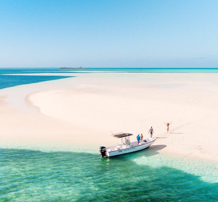 Small boat near a white sandbar in turquoise shallow water under a clear blue sky