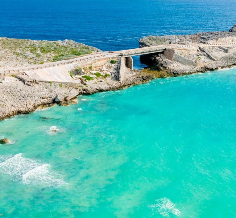 Turquoise cove beside a rocky coast with a narrow road bridge over the water