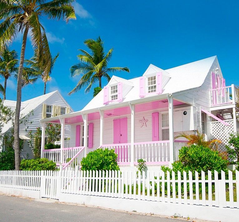 Pink and white beach cottage with palm trees and a white picket fence under a bright blue sky