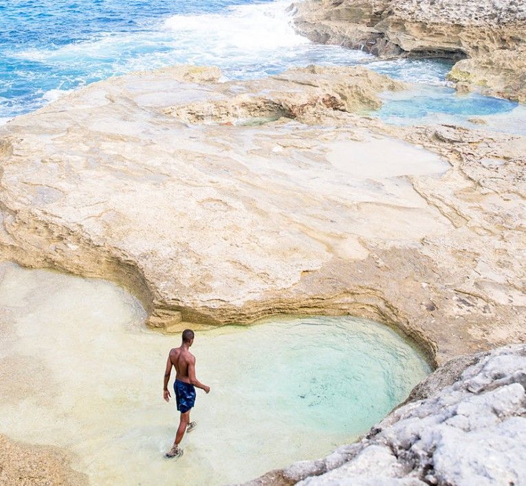 Person standing in a turquoise tidal pool beside rocky shoreline and ocean waves