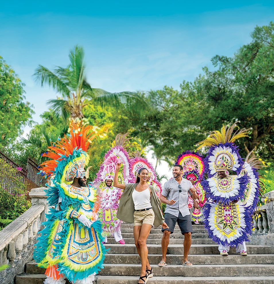 Tourists walking down steps beside colorful feather dancers in a tropical outdoor setting