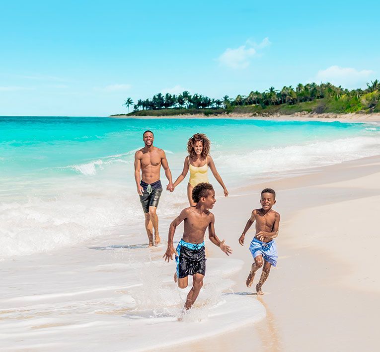 Family running along a sunny tropical beach with turquoise water and palm trees
