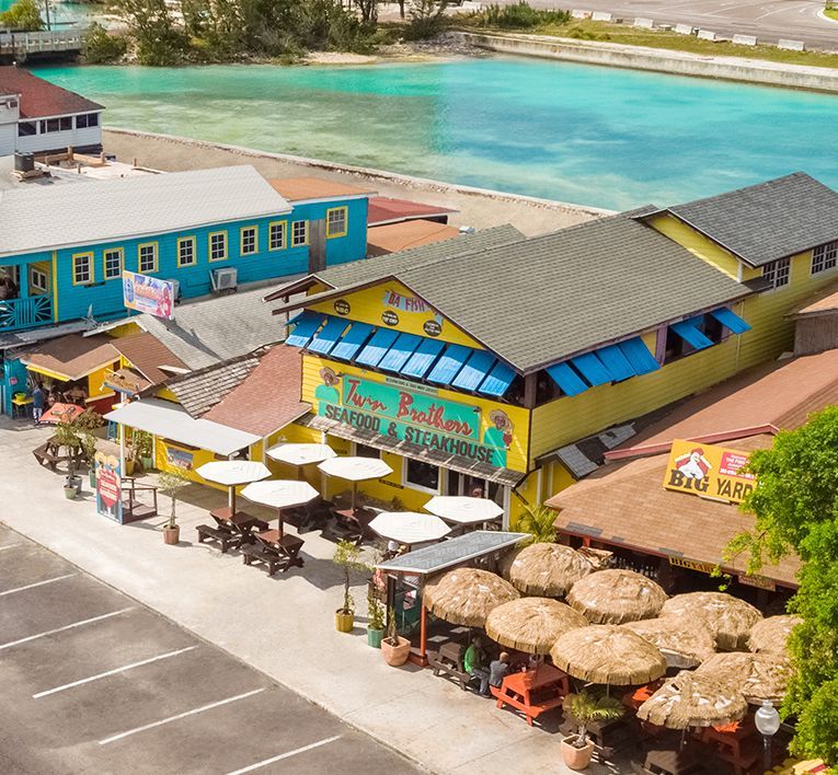 Aerial view of colorful beachside restaurants with outdoor umbrellas beside turquoise water