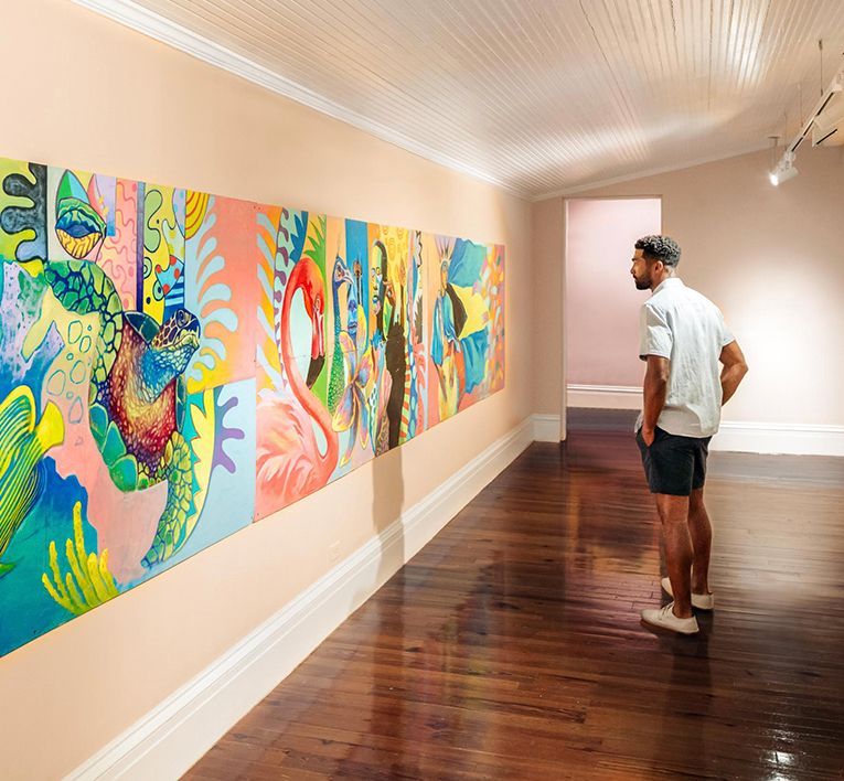 Person viewing colorful abstract paintings in a gallery with polished wooden floors.