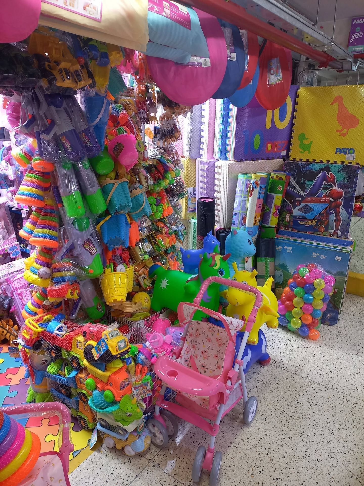 Un colorido puesto de juguetes repleto de juguetes colgantes, animales de peluche y un cochecito infantil rosa.