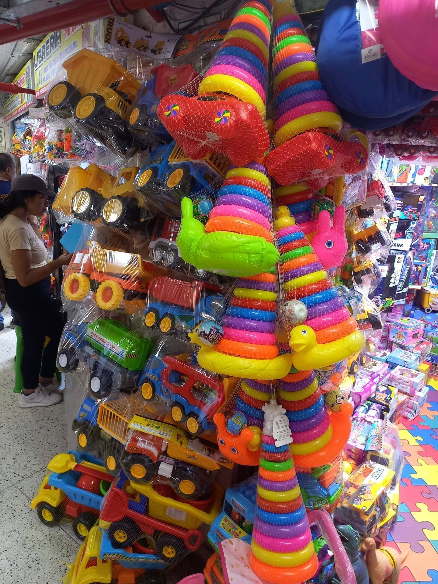 Peluches y animales de peluche coloridos con rayas de arcoíris cuelgan en un puesto de juguetes abarrotado.