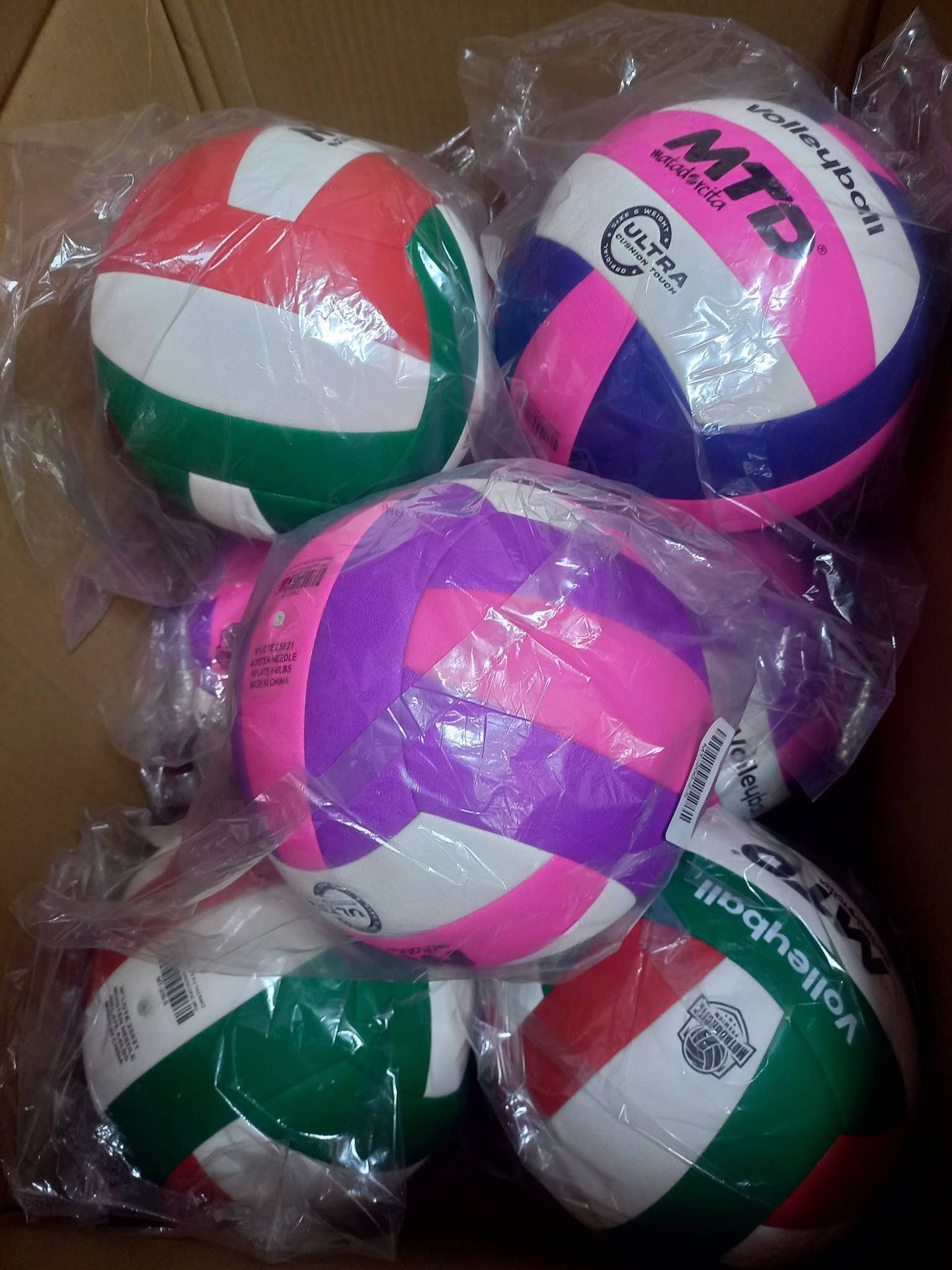 Pila de coloridos balones de voleibol MVA envueltos en plástico: rojo, verde, rosa, blanco y morado.