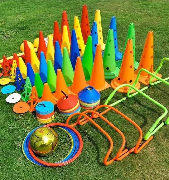Conos, vallas y pelotas de entrenamiento deportivo de colores, dispuestos sobre césped al aire libre.