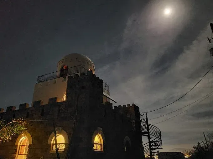 Night view of a castle-like building with a round dome, lit windows, and a spiral staircase under a full moon.