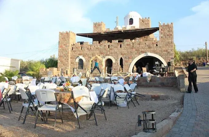 Outdoor event with white tables and chairs in front of a stone building with archways and a dome.