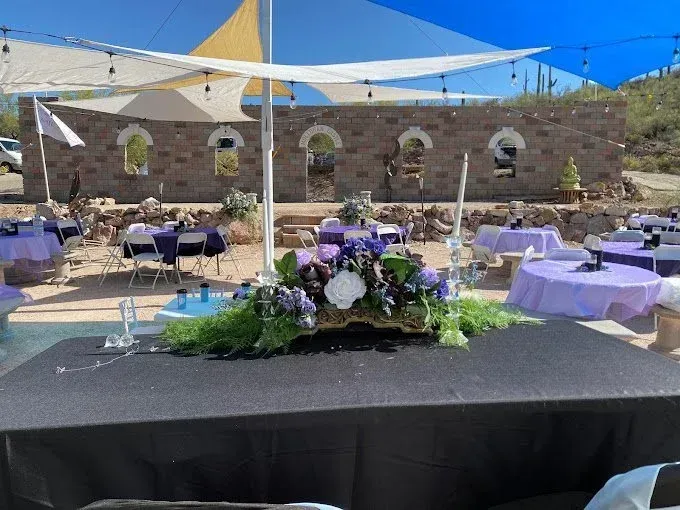 Outdoor event setup with purple accents and a stone backdrop under shade sails.
