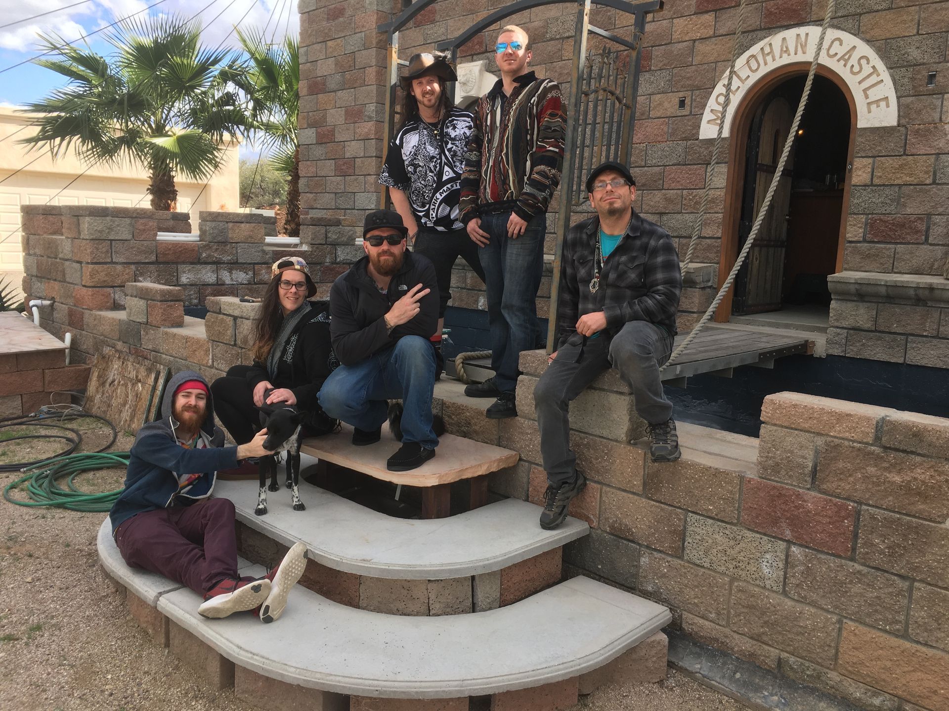 Group of people posing by a brick castle entrance. One person has a goat on a leash.