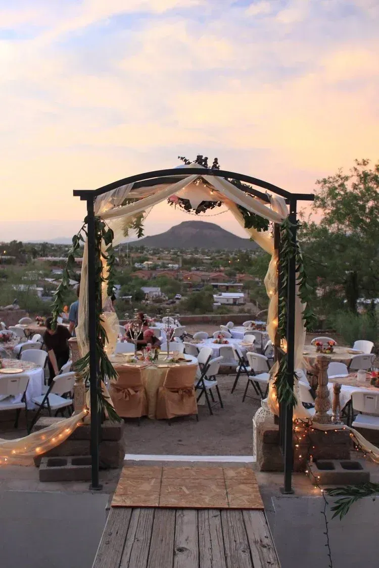 Wedding arch overlooking a landscape at sunset; tables are set for a reception.