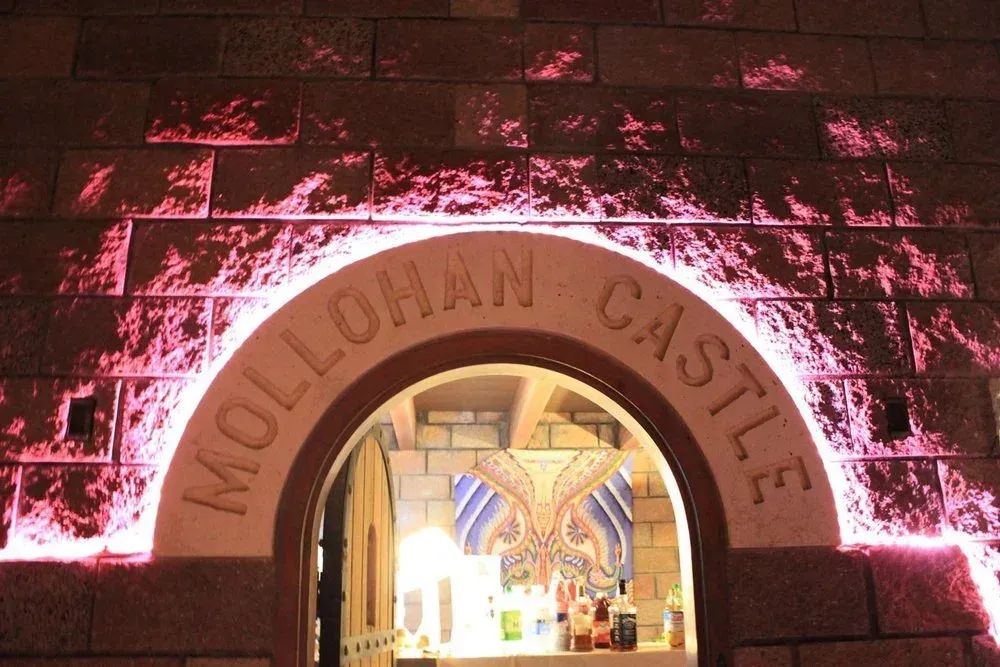 Archway entrance to Mollohan Castle, with red lighting and carved lettering. Interior visible.