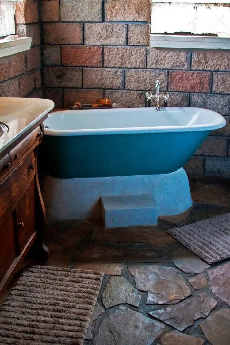 Blue bathtub in a rustic bathroom with stone flooring and brick walls.