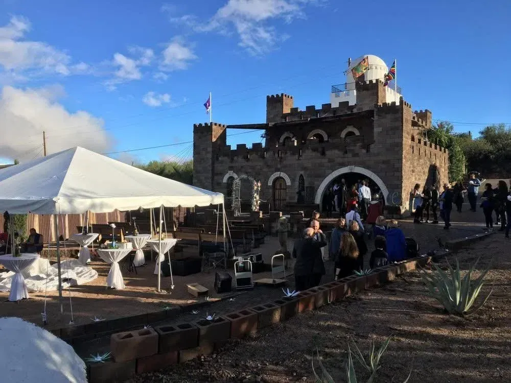 Castle-like building with a white tent set up outside; people gathered for an event under a blue sky.