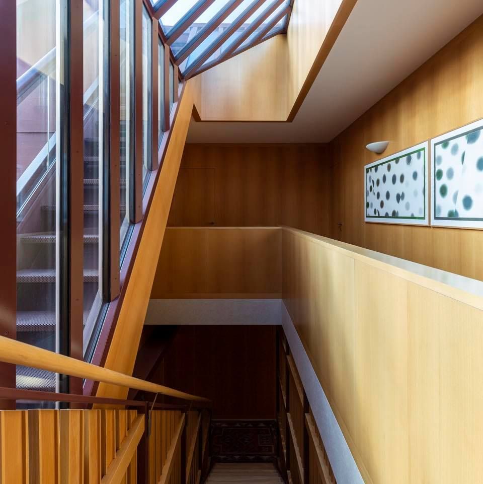 Vano scale interno moderno con pannelli in legno, ringhiere in vetro e lucernario sul soffitto.