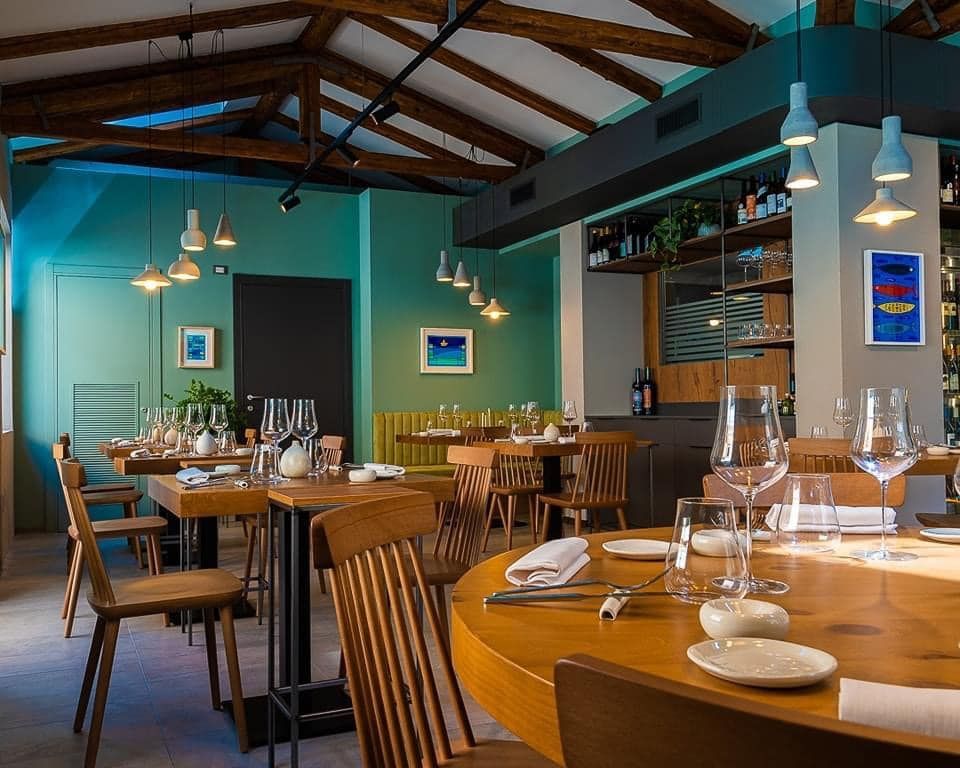 Sala da pranzo moderna del ristorante con tavoli e sedie in legno e pareti blu-verdi sotto travi a vista sul soffitto.