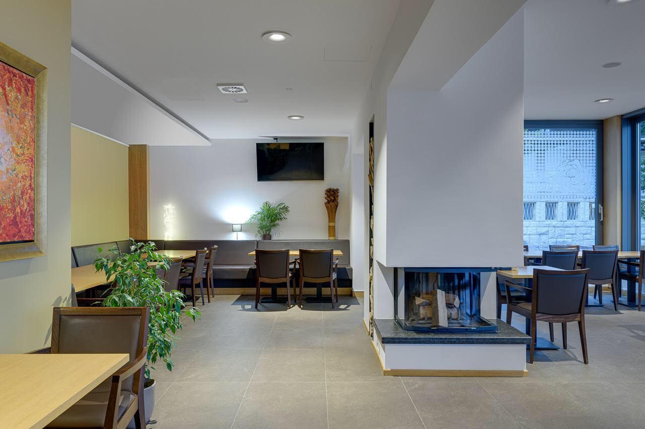 Moderna sala d'attesa con tavoli, sedie, piante e TV a parete.