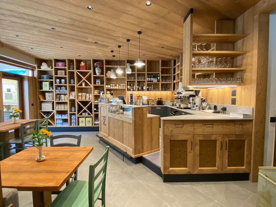 Accogliente interno di caffetteria con scaffali, bancone e tavoli in legno sotto un soffitto inclinato in legno.