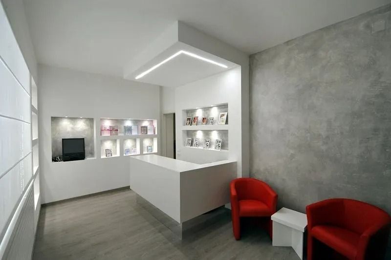 Sala d'attesa moderna e minimalista di colore bianco con scaffali a muro e sedie rosse.