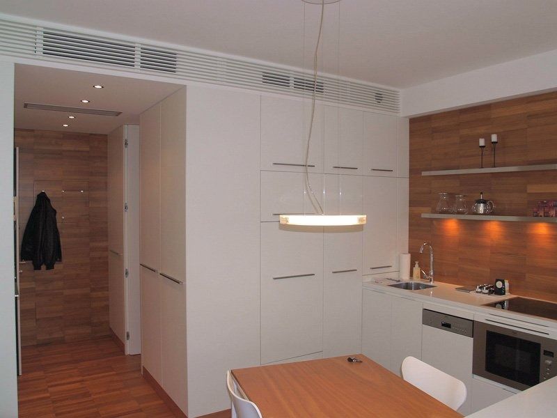Cucina moderna con mobili bianchi, dettagli in legno, tavolo da pranzo e lampada a sospensione.