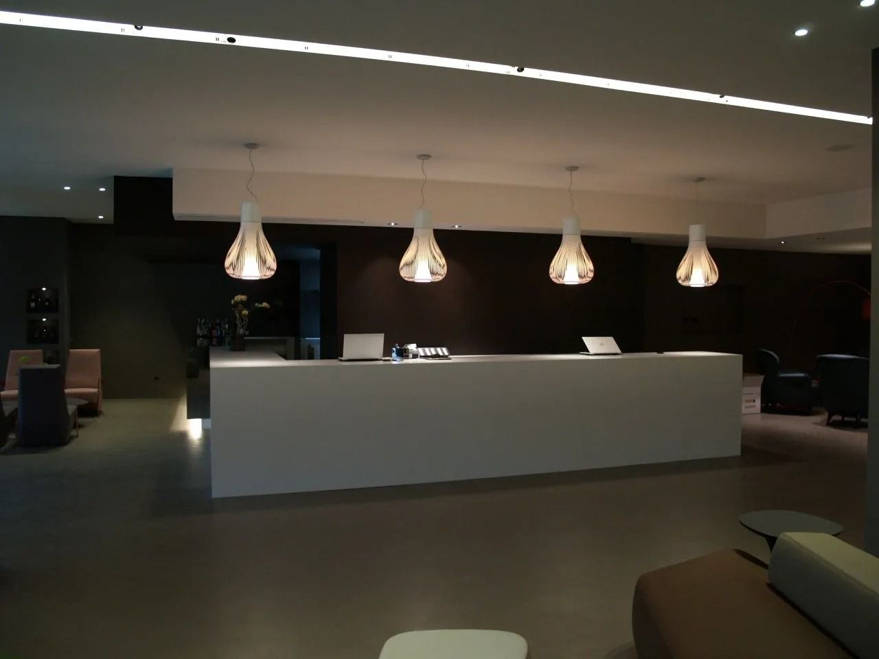 Atrio moderno e poco illuminato dell'hotel con bancone della reception bianco e quattro lampade a sospensione sopra di esso.