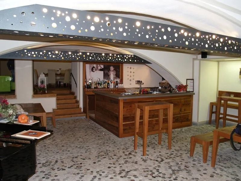 Moderno bar seminterrato con bancone in legno, sgabelli, scala e lampade decorative ad arco sul soffitto.