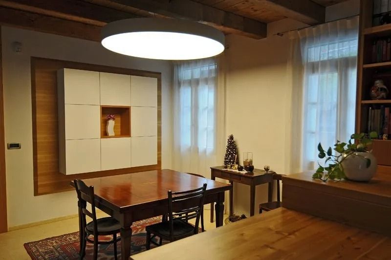 Accogliente sala da pranzo con tavolo e sedie in legno, travi a vista e alte finestre che lasciano entrare una luce soffusa.