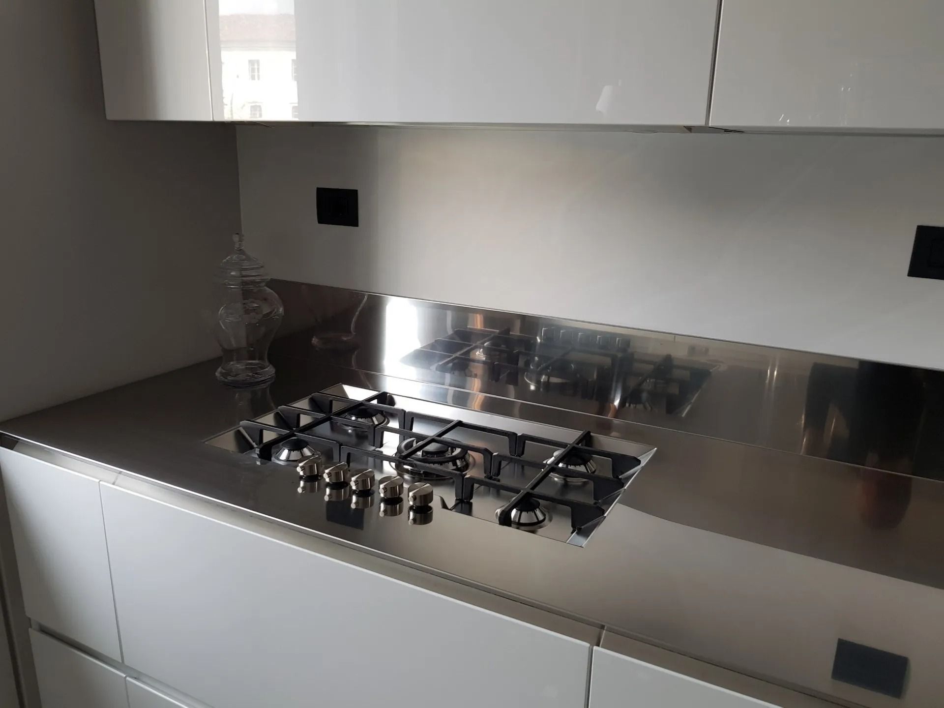 Cucina moderna con piano di lavoro in acciaio inox e piano cottura a gas integrato sotto un pensile.