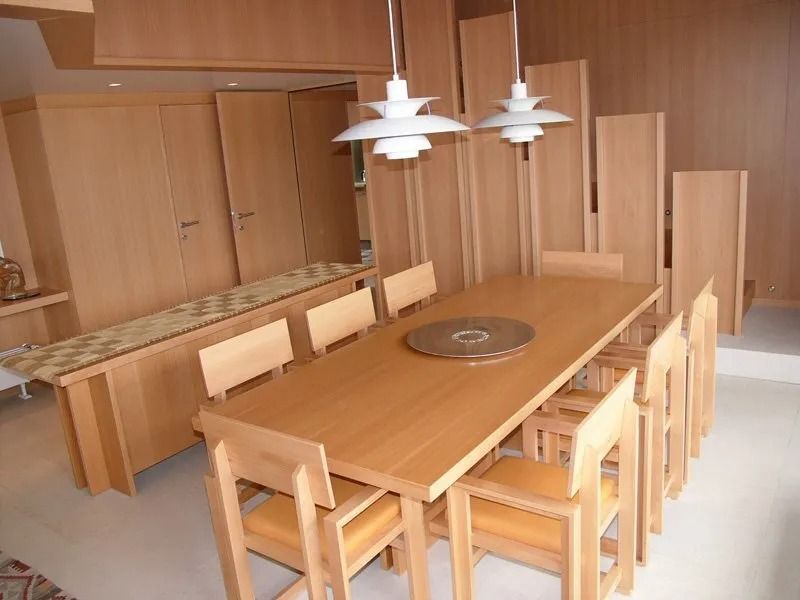 Sala conferenze moderna in legno con lungo tavolo, sedie abbinate e lampade a sospensione.