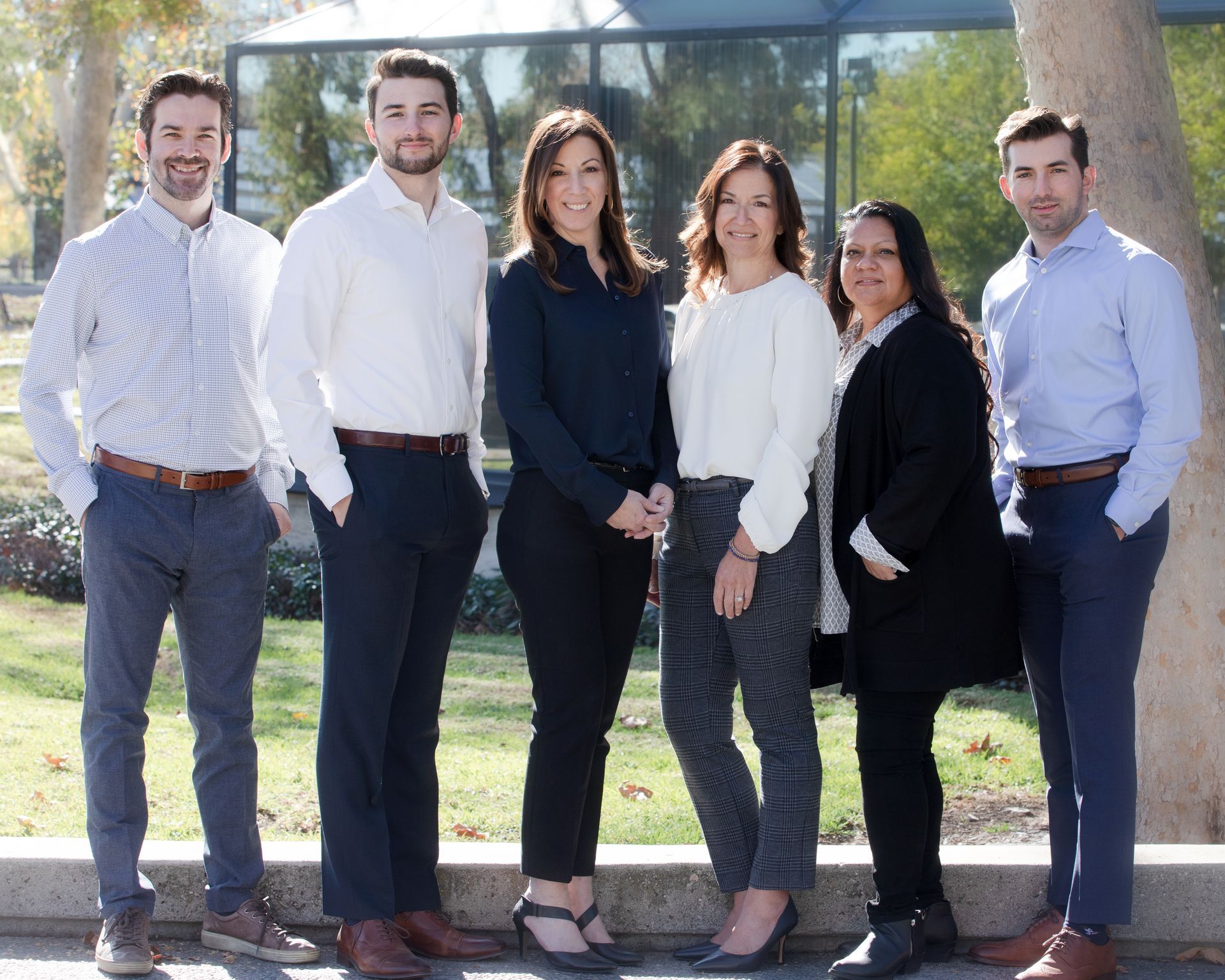 Six people standing outdoors in front of a building, dressed in business attire.