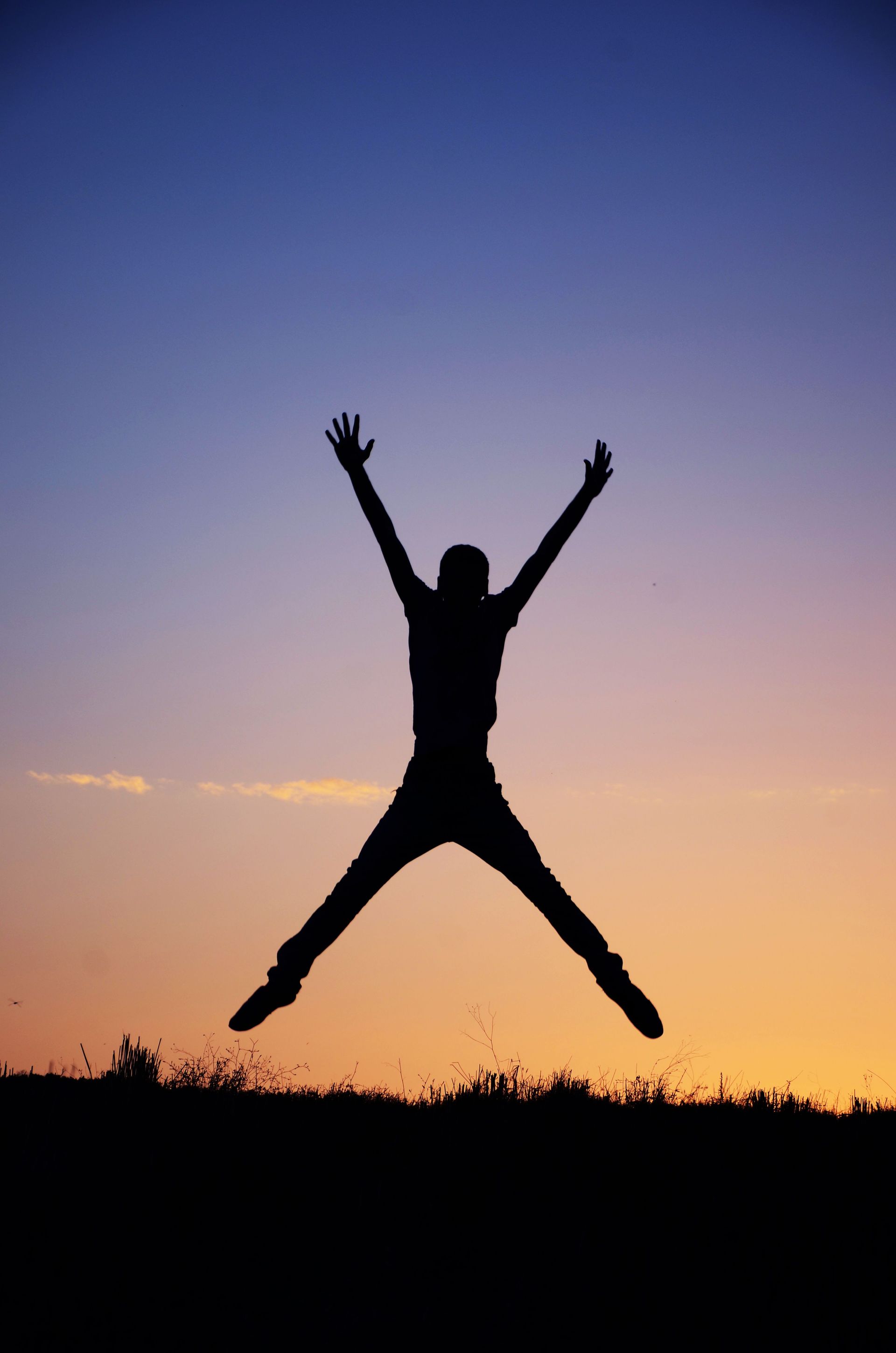 Silhouette of a person jumping with arms and legs spread against a sunset sky