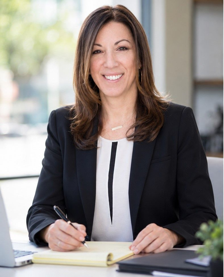 Smiling professional at a desk, writing in a notebook in an office setting.