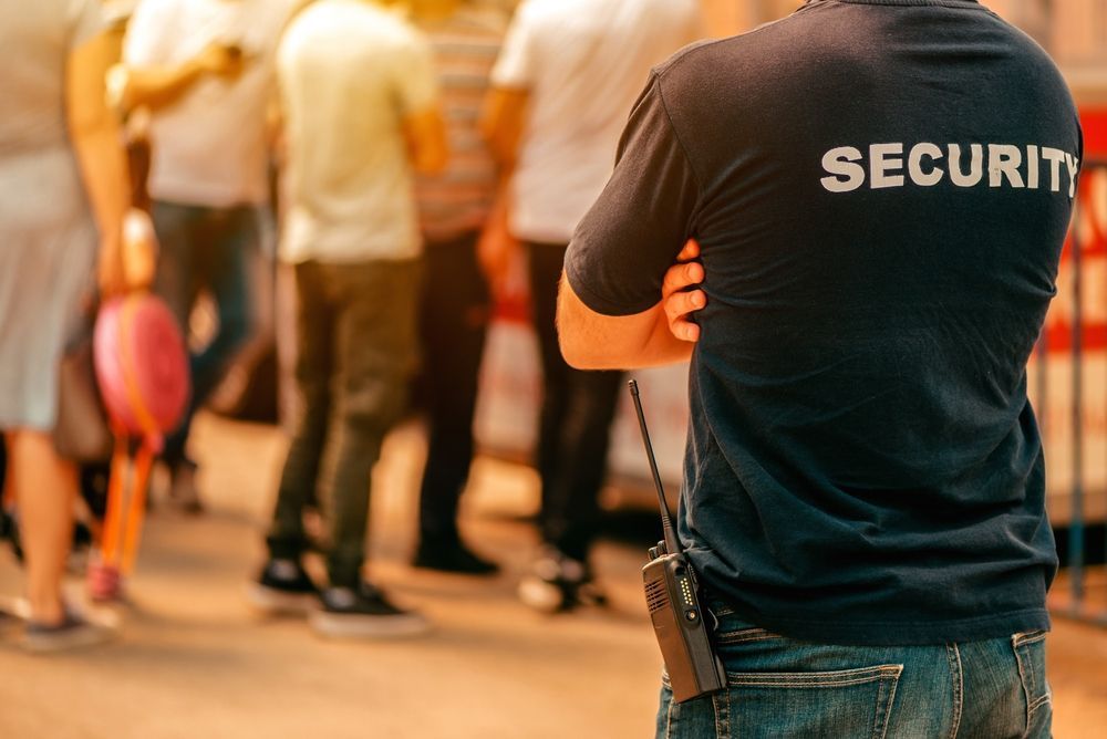 Security guard standing with arms crossed in a busy indoor crowd area