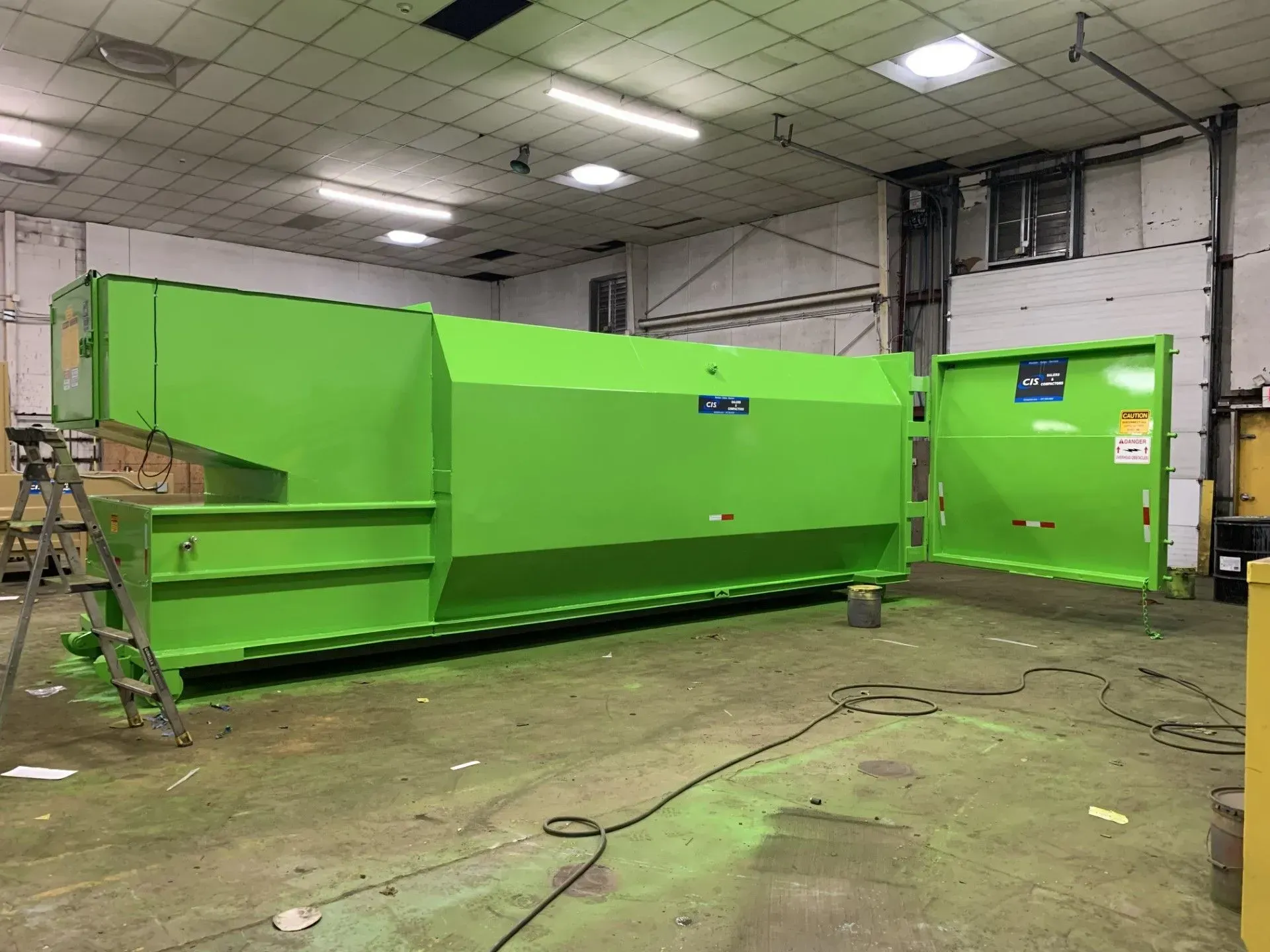 Large, bright green industrial compactor inside a warehouse. 