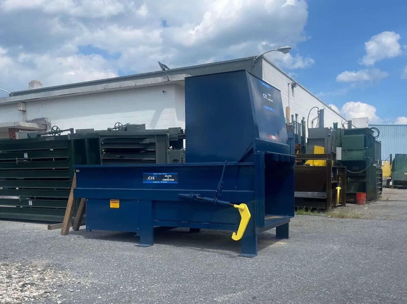 Blue industrial baler machine outside a building on a cloudy day.