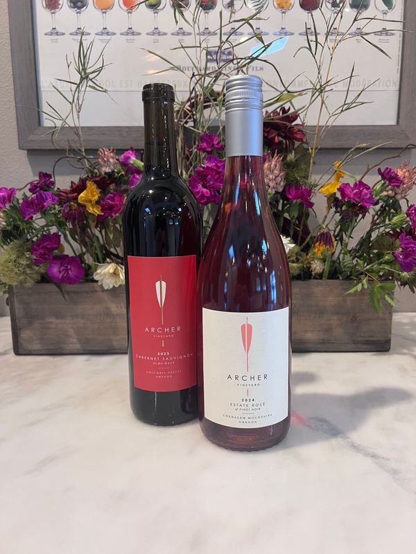 Two wine bottles on a marble counter before a colorful floral arrangement and framed botanical print.