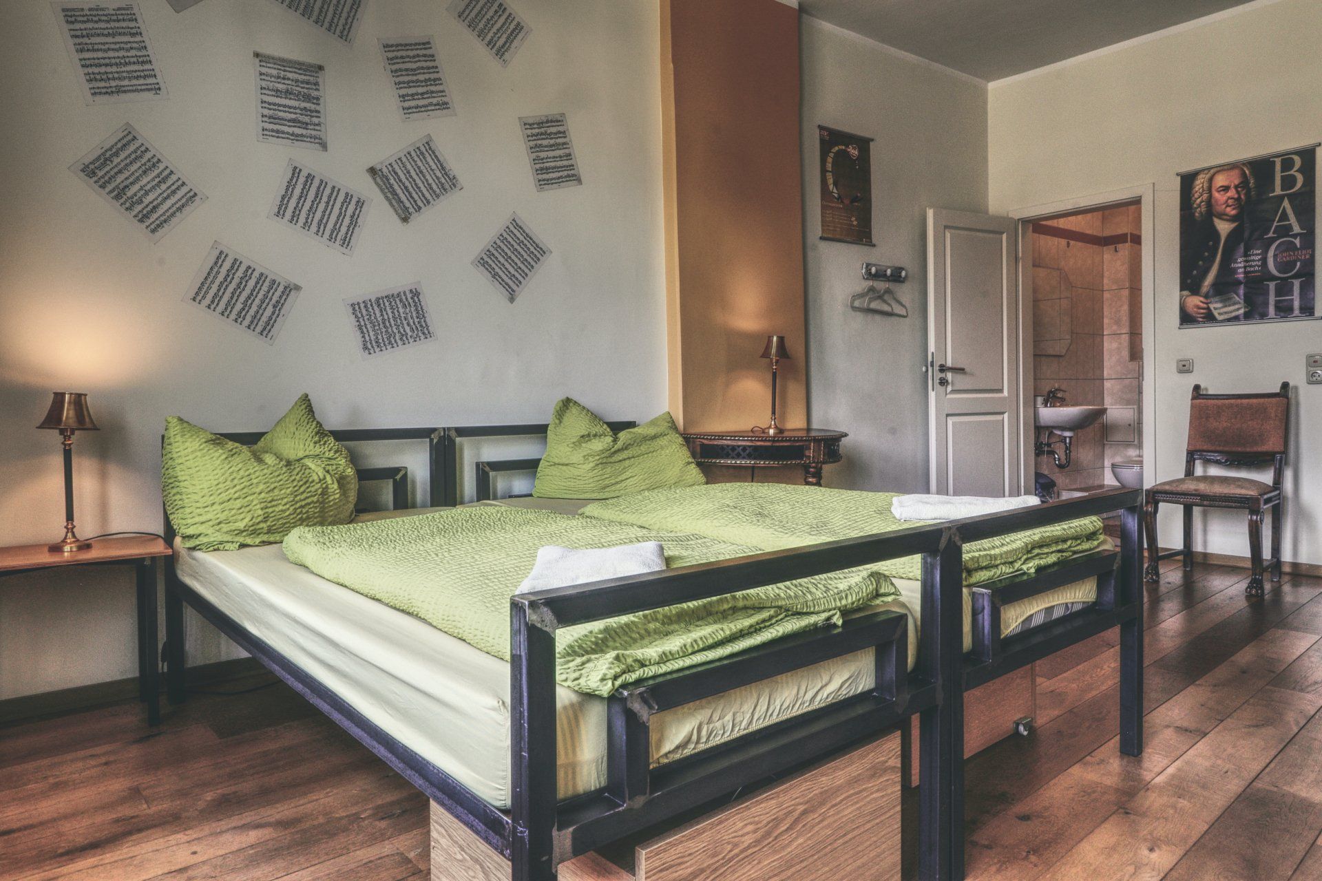Gemütliches Doppelzimmer mit grüner Bettwäsche und Wanddeko aus Notenblättern und eigenem Bad im OPERA Hostel Erfurt
