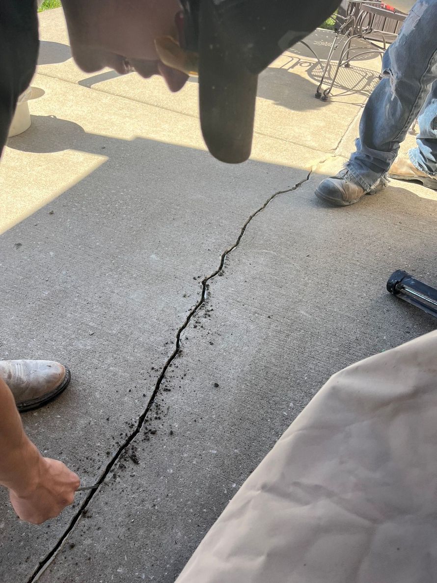 Cracked concrete pavement with several people standing around it, including a person in jeans and boots.