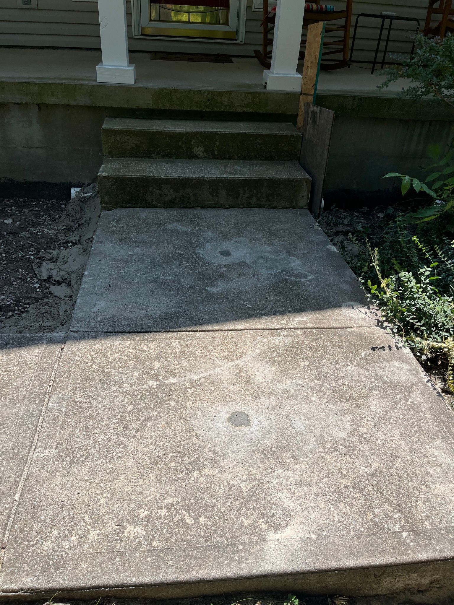 Concrete walkway leading to front steps of a house with porch columns and a garden bed beside it