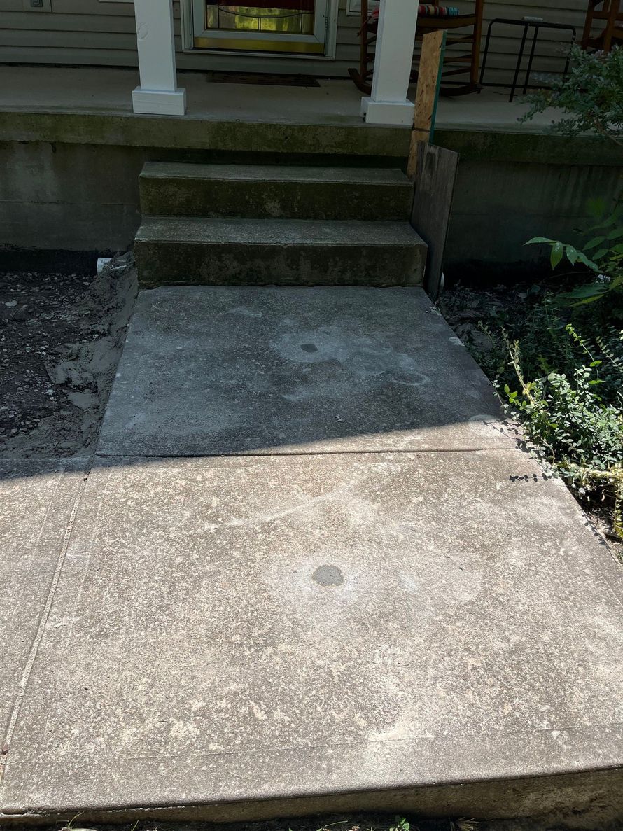 Concrete walkway leading to three porch steps with white columns and a dark front entry.