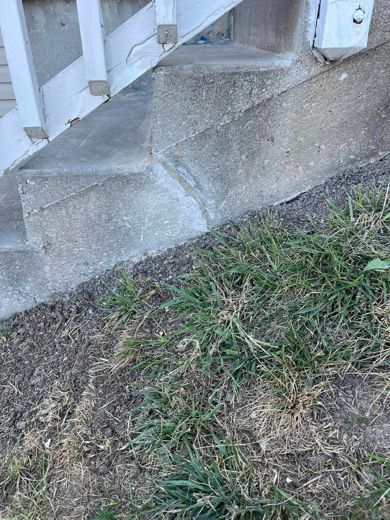 Concrete steps beside a patchy grass lawn and mulch near a white porch railing