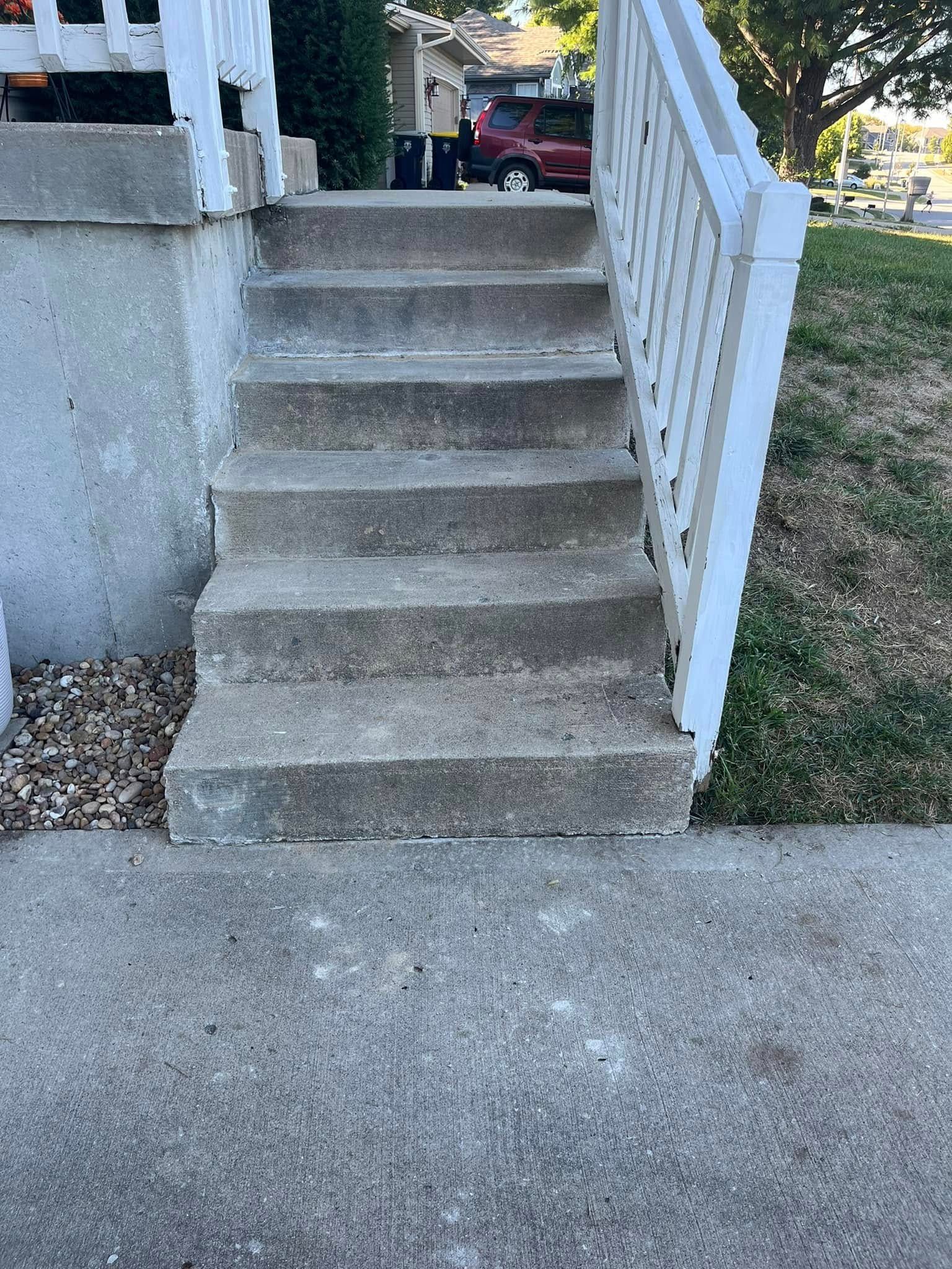 Concrete front steps with a white handrail leading up to a porch.
